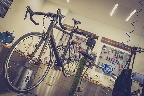A road bike hanging on a bicycle repair stand inside of a workshop.