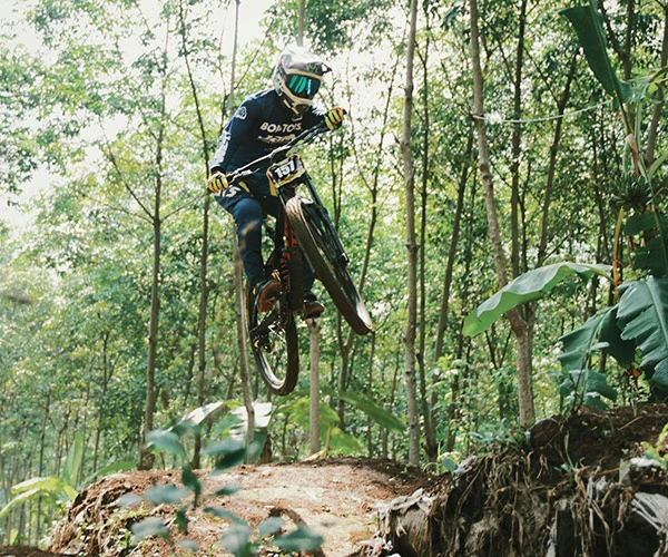 A man mid air over a dirt jump riding a mountain bike dirt jumper bicycle.
